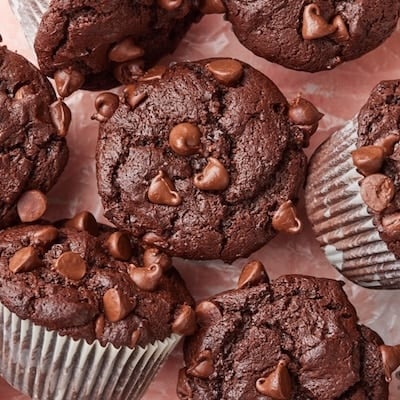 Top view of homemade bakery-style double chocolate chip muffins with domed tops and melty chocolate chips arranged on parchment paper.