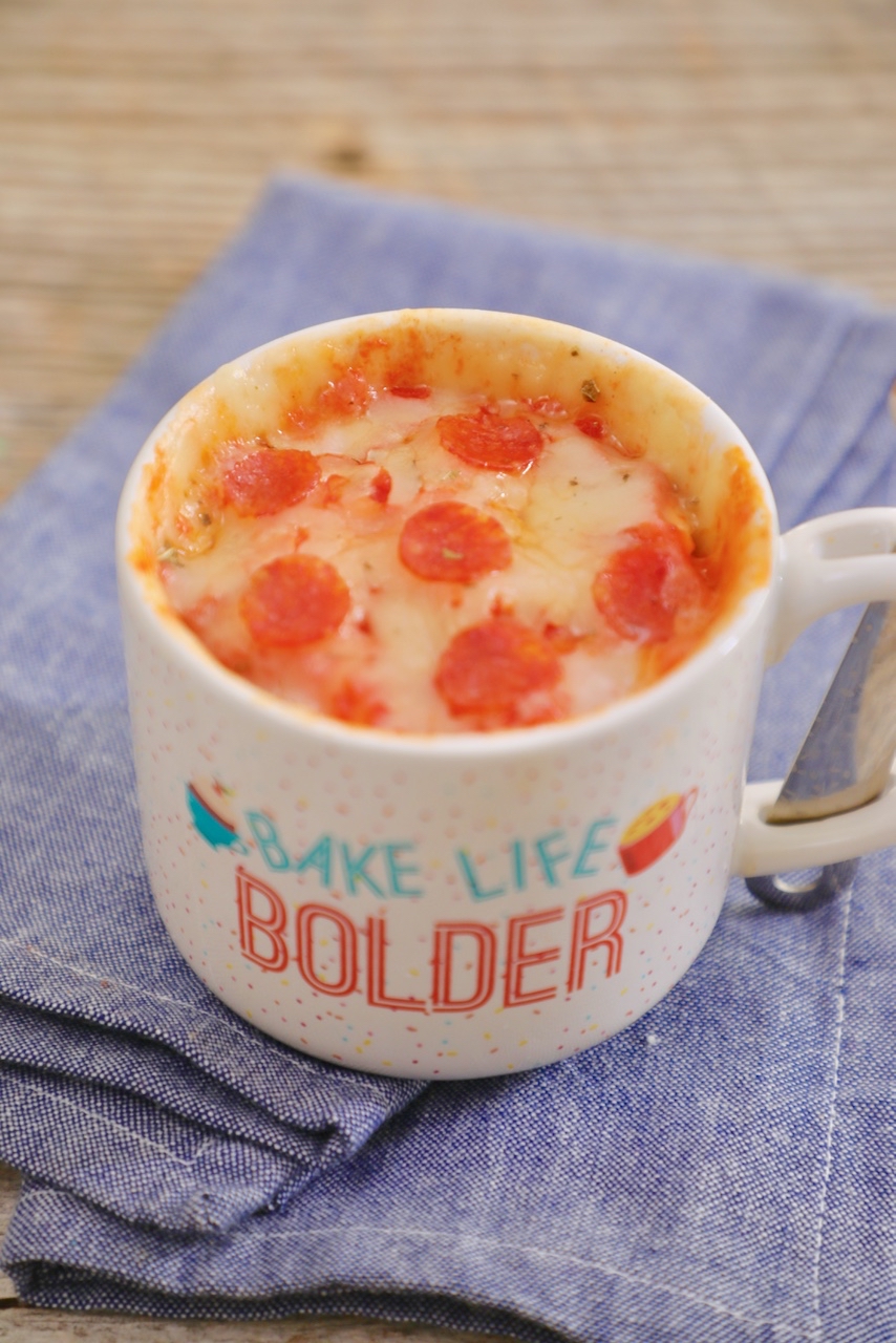 A single serving pizza made in the microwave and baked in a mug, topped with cheese and pepperonis.