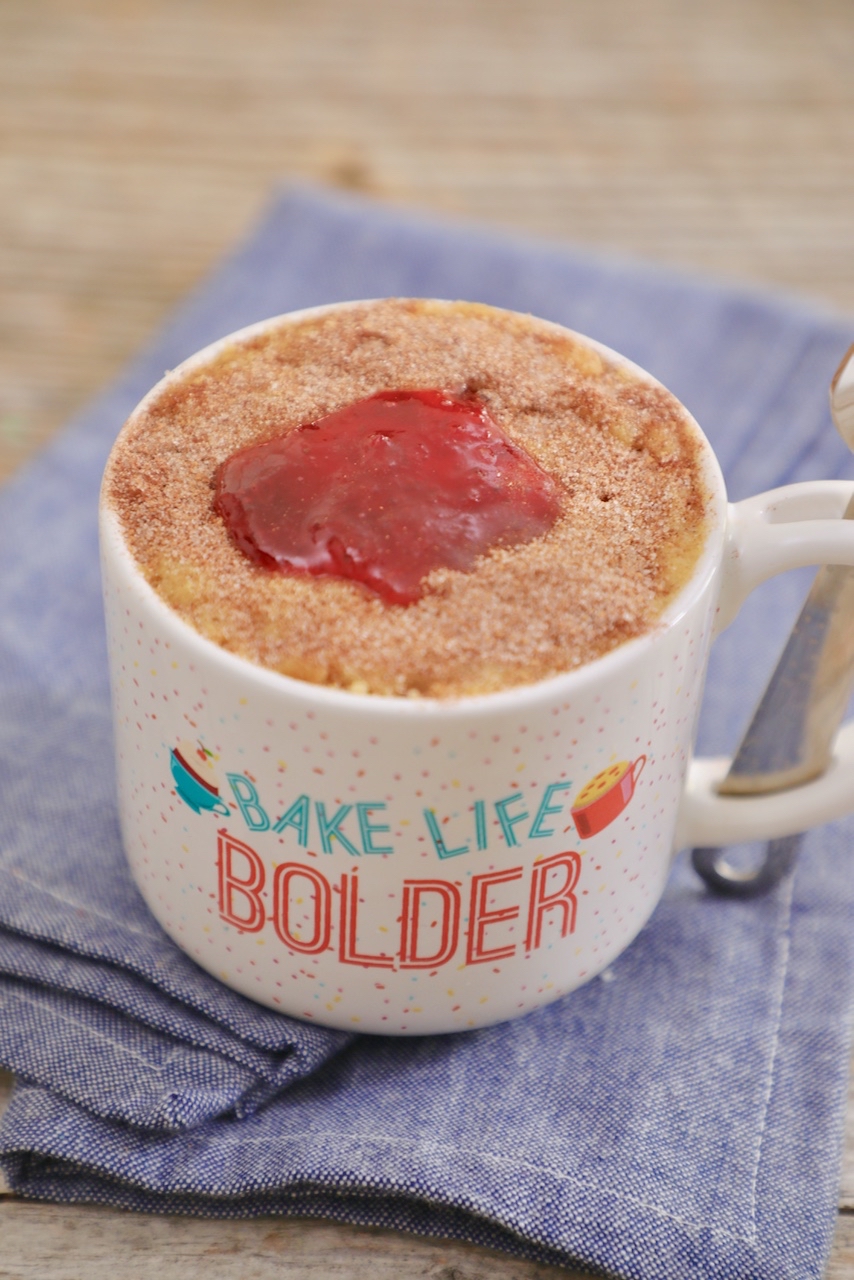 A fully baked jelly donut in a mug, topped with jam and cinnamon sugar.