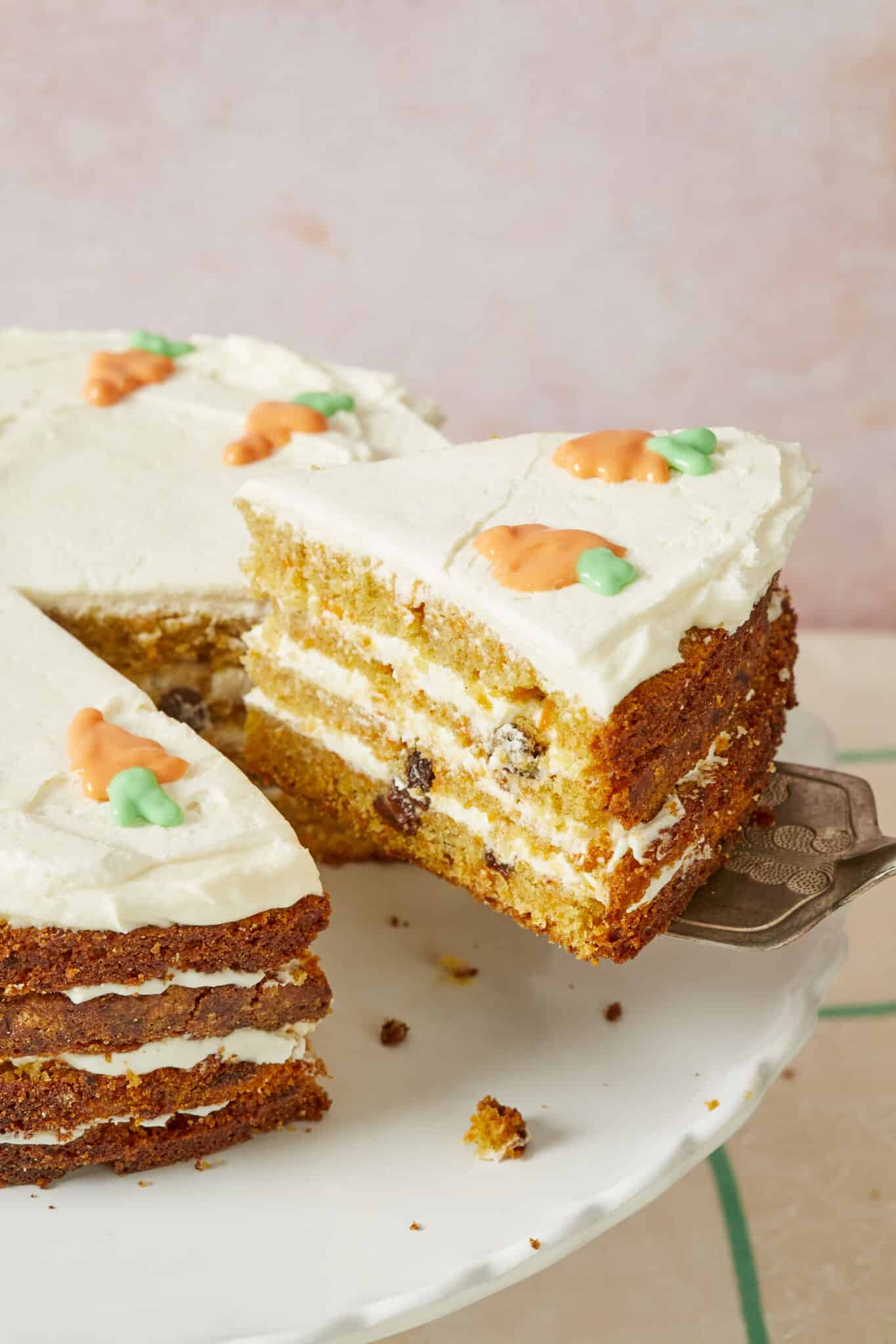 A slice of Best-Ever Carrot Cake has been cut and is being lifted with a serving spatula. The cakes moist and loaded with raisins, layered in between and covered with cream cheese frosting. 