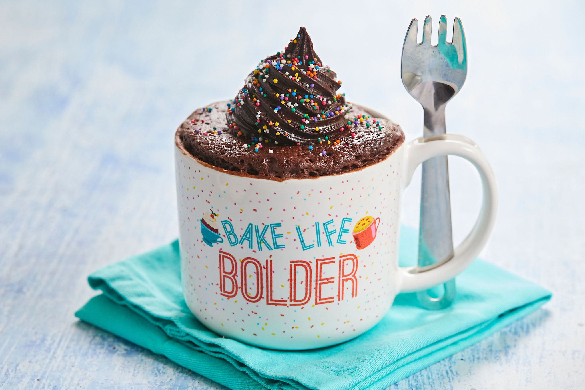 My Best-Ever Chocolate Mug Cake piled high with frosting in my Bigger Bolder Baking Mug Meals Mug with Spork!