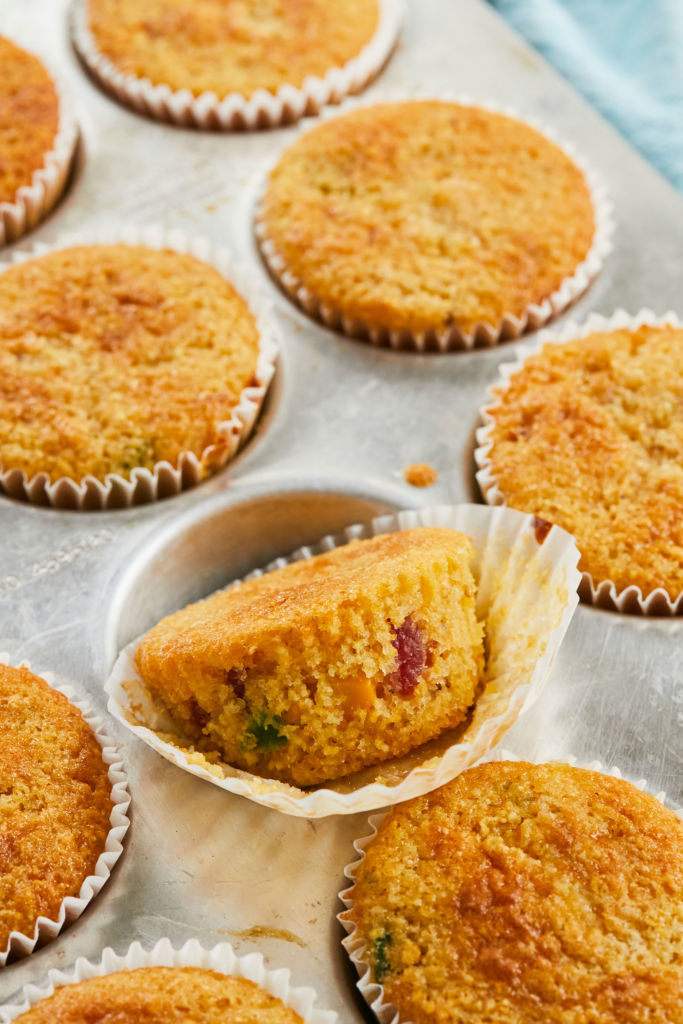 A tin of cornbread muffins, one unwrapped to show texture and fillings.