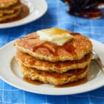 A stack of fluffy oat flour pancakes served with maple syrup, butter and orange juice.