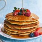 A fresh stack of Gluten-Free Pancakes with berries and syrup.