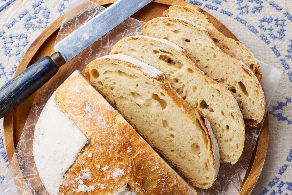 Half loaf of golden sourdough bread with four slices on the side. It has bubbly open crumb and golden crispy crust)