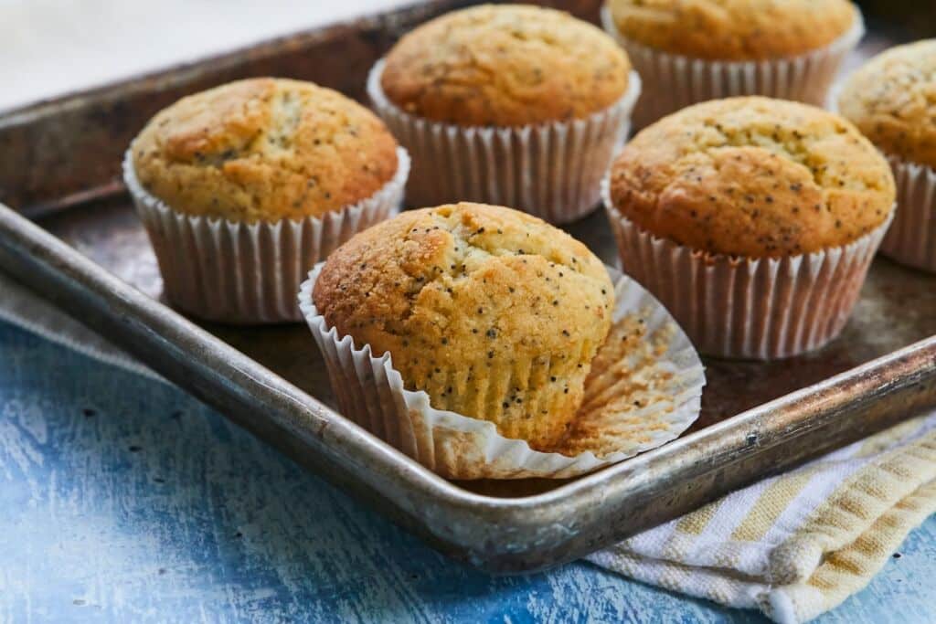 Lemon Poppy Seed muffins in paper liners on a baking sheet.
