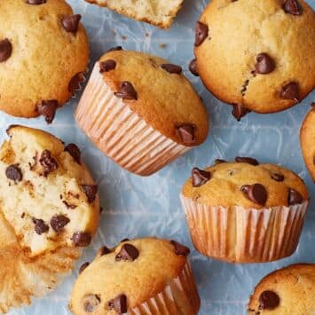 Homemade chocolate chip muffins with golden domed tops and chocolate chips, including one muffin split open to reveal a soft, fluffy crumb studded with melted chocolate chips.