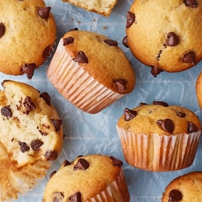 Homemade chocolate chip muffins with golden domed tops and chocolate chips, including one muffin split open to reveal a soft, fluffy crumb studded with melted chocolate chips.