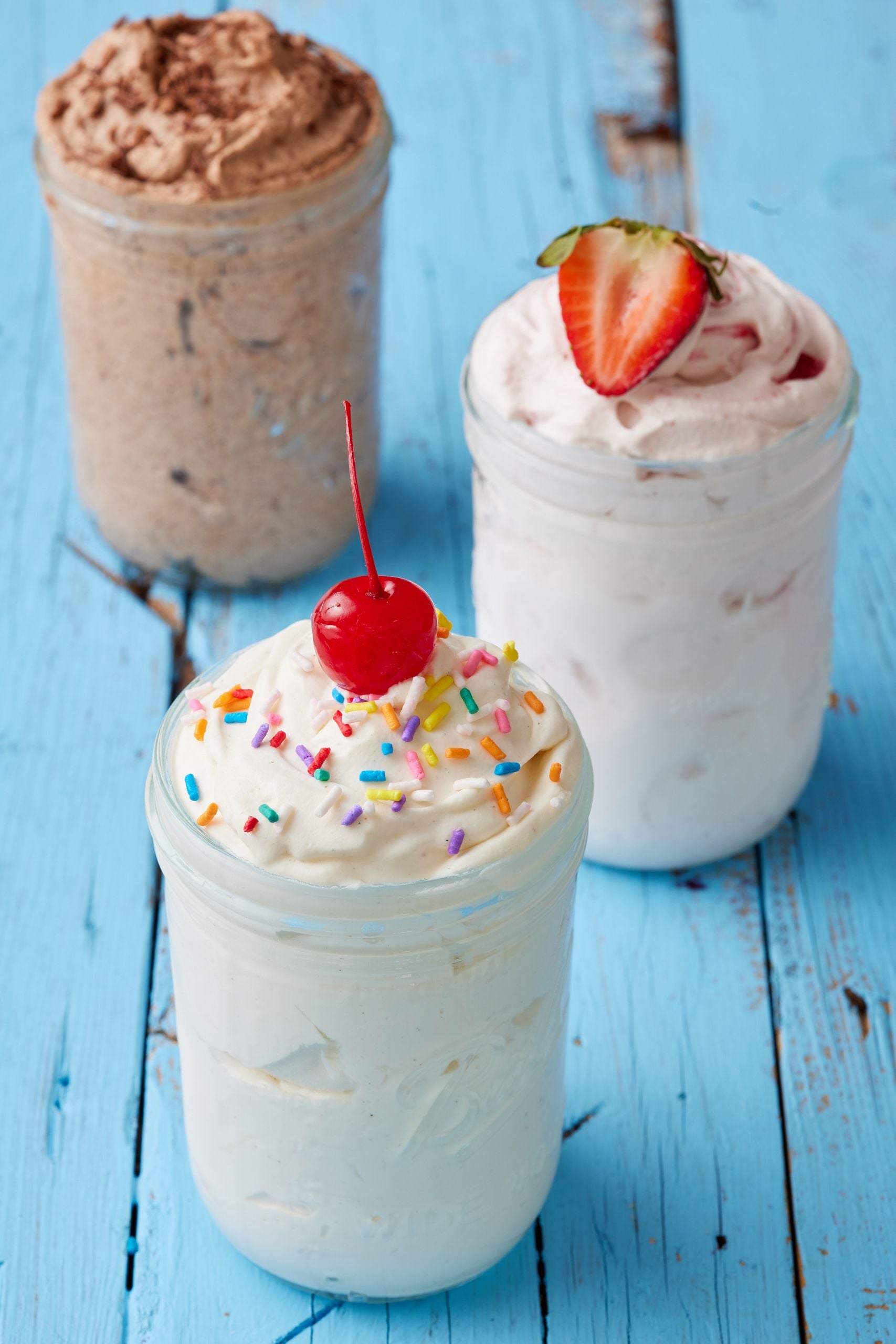 Mason Jar Ice Cream in vanilla flavor with sprinkles, strawberry flavor with half strawberry, and chocolate flavor.