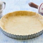 A gluten-free pie crust, ready for filling, flanked by a rolling pin and shaker.
