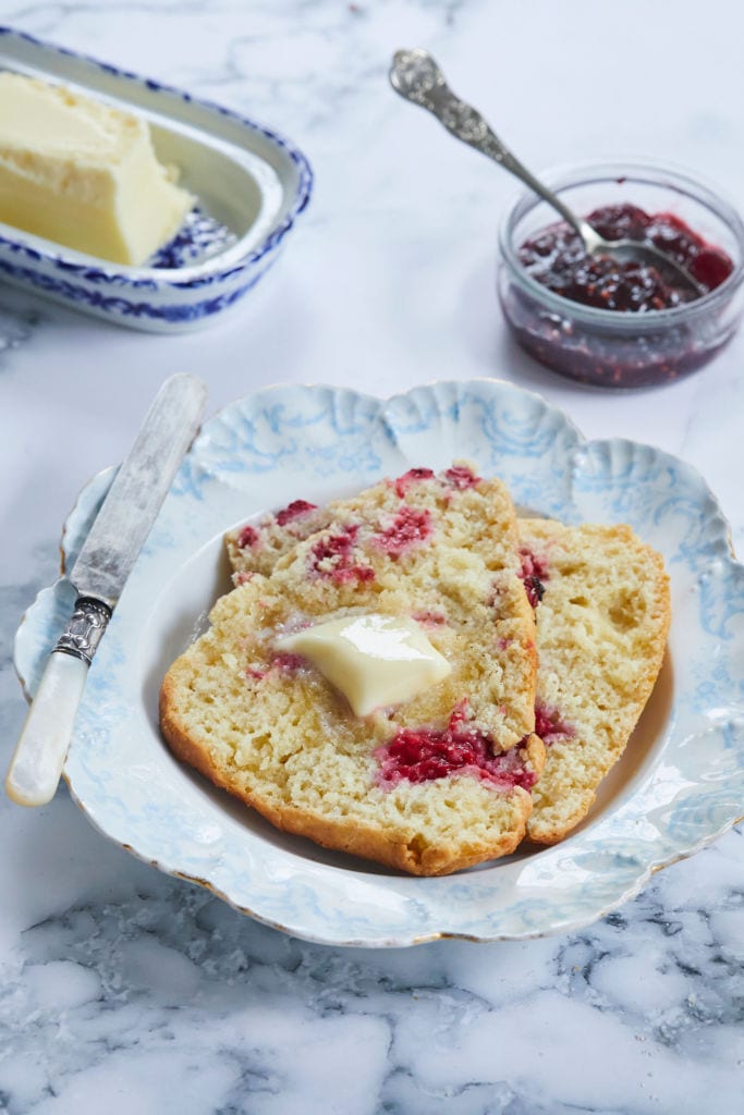 Raspberry Scones cut open to show consistency and texture, topped with butter.