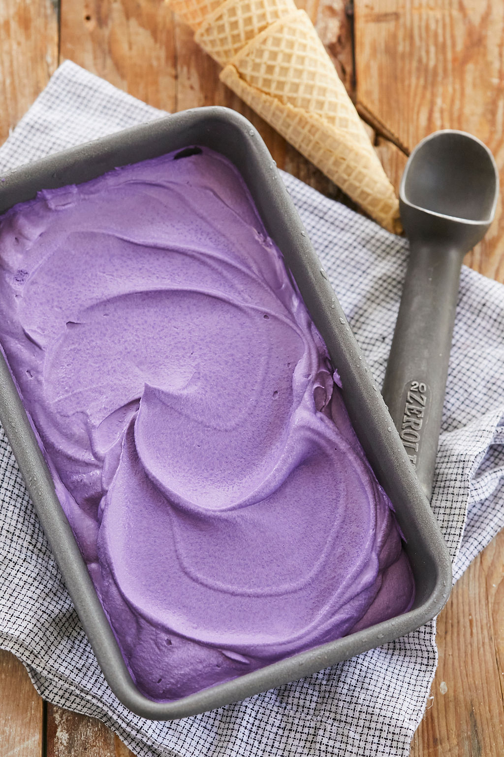 Bright purple easy Ube Ice Cream recipe, top-down, next to cones and a scoop.