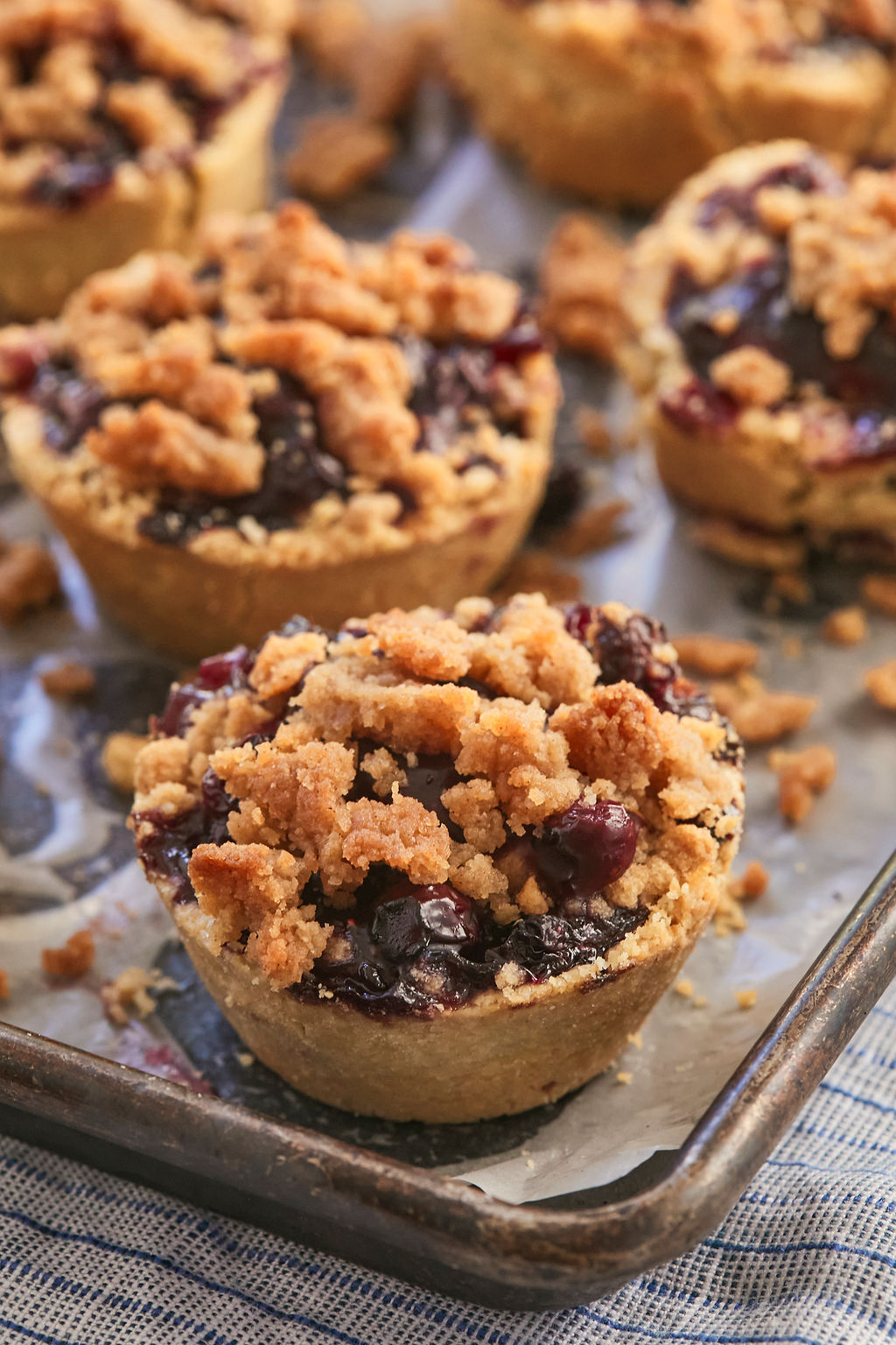 Mini blueberry pies with a cinnamon crumb topping on a baking pan.