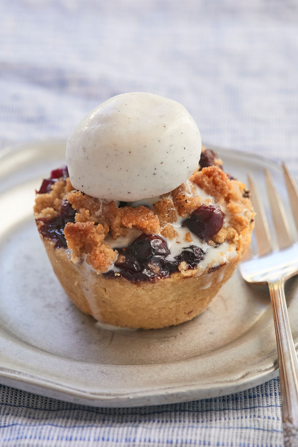One Blueberry Crumb Pie topped with vanilla bean ice cream on a plate with a fork ready to take a bite.