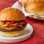 A burger made with golden and fluffy Brioche Hamburger Buns, with extra buns in the back.
