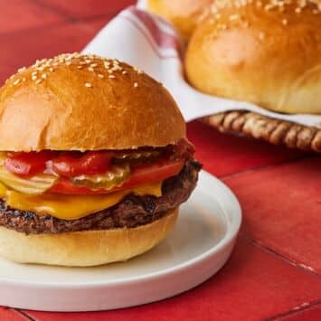 A burger made with golden and fluffy Brioche Hamburger Buns, with extra buns in the back.