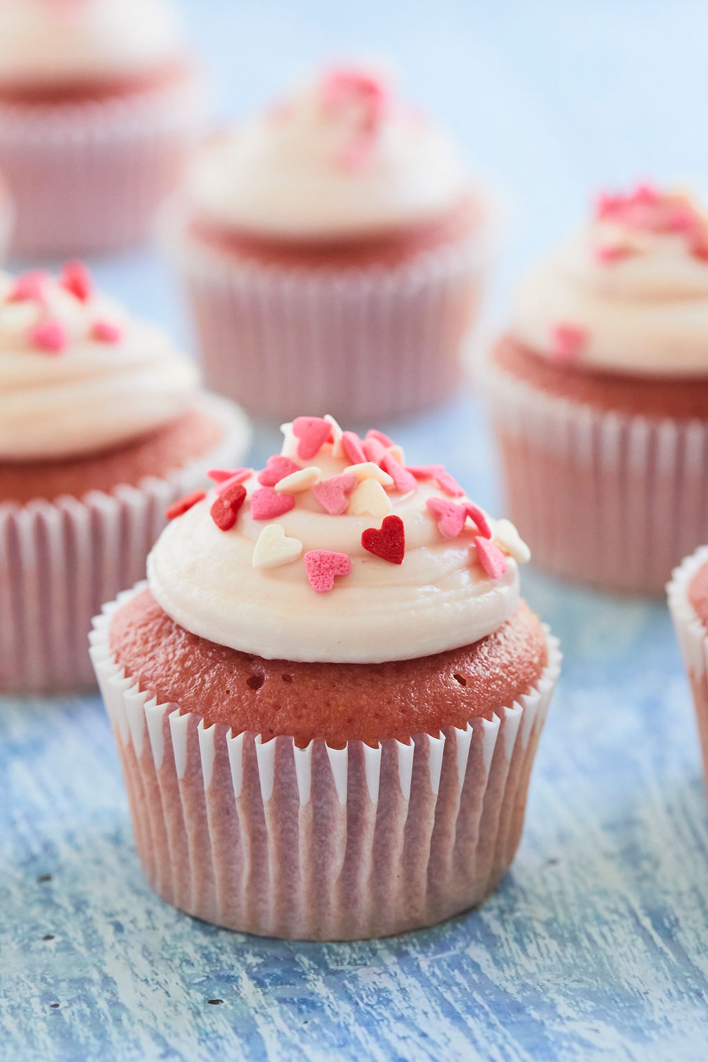 A strawberry cupcake topped with strawberry cream cheese frosting, and heart sprinkles.