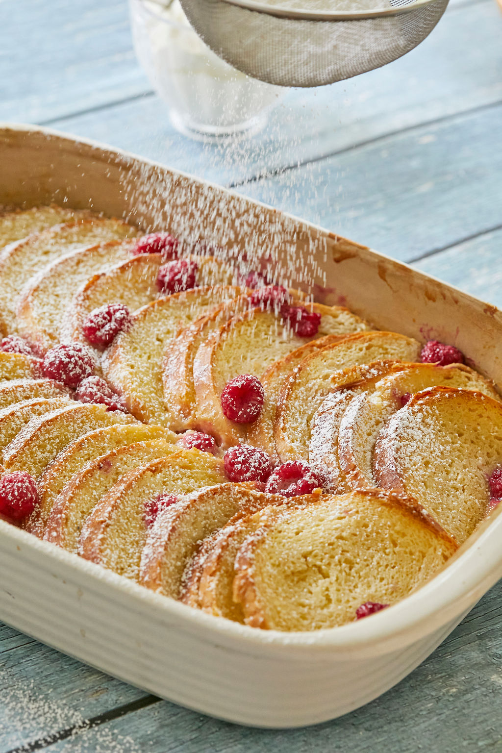 White Chocolate, Whiskey, and Raspberry Bread Pudding being dusted with powdered sugar.