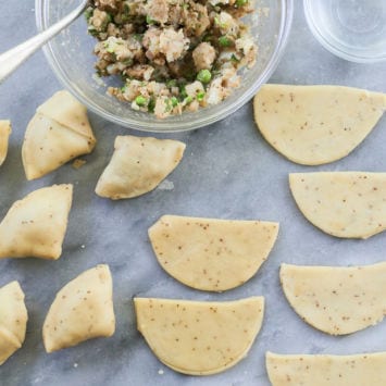 Samosas ready for baking and ready to be made, laid out on a table with a bowl of vegan samosa filling