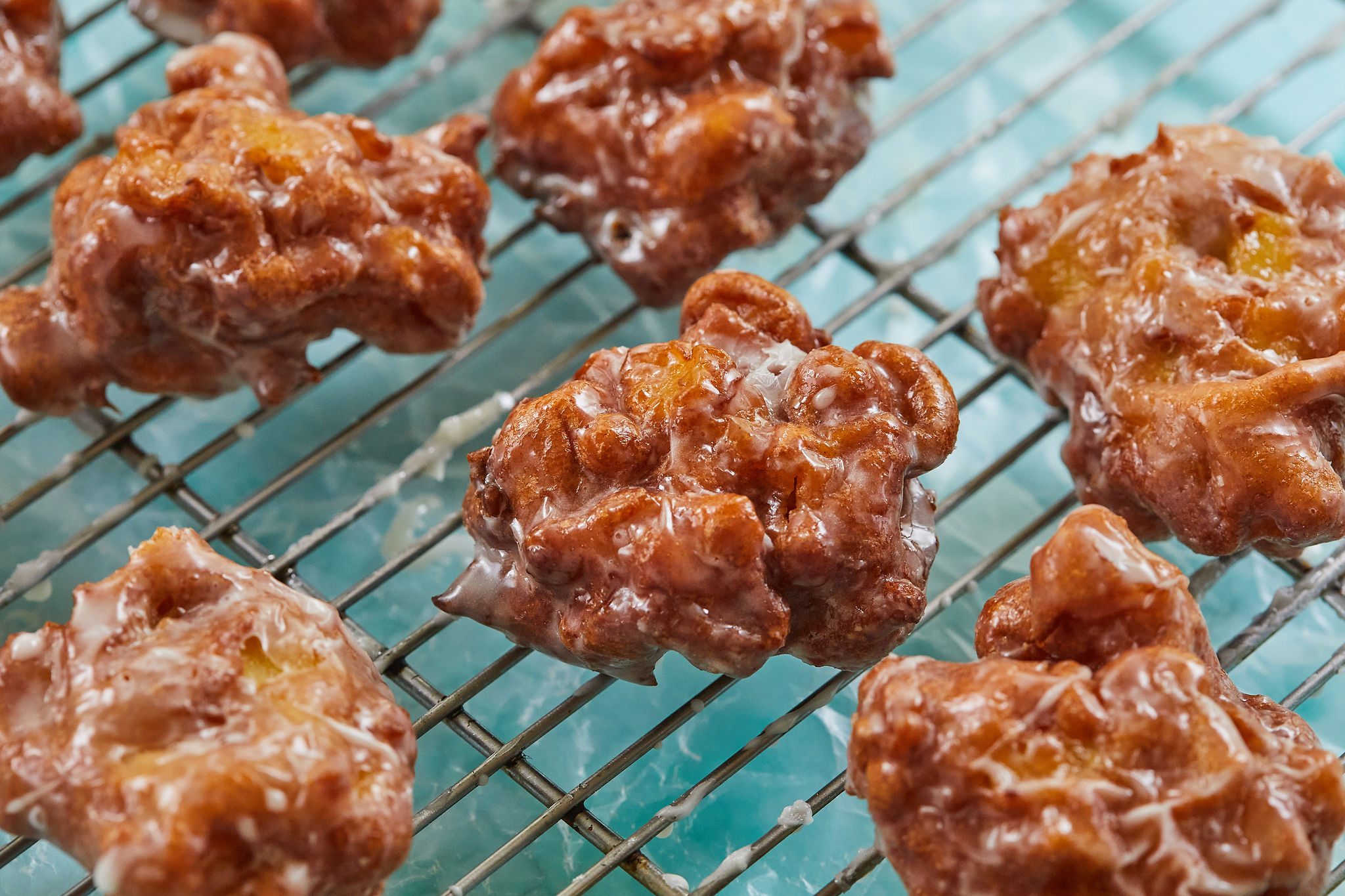 A bunch of apple fritters cooling on a rack.