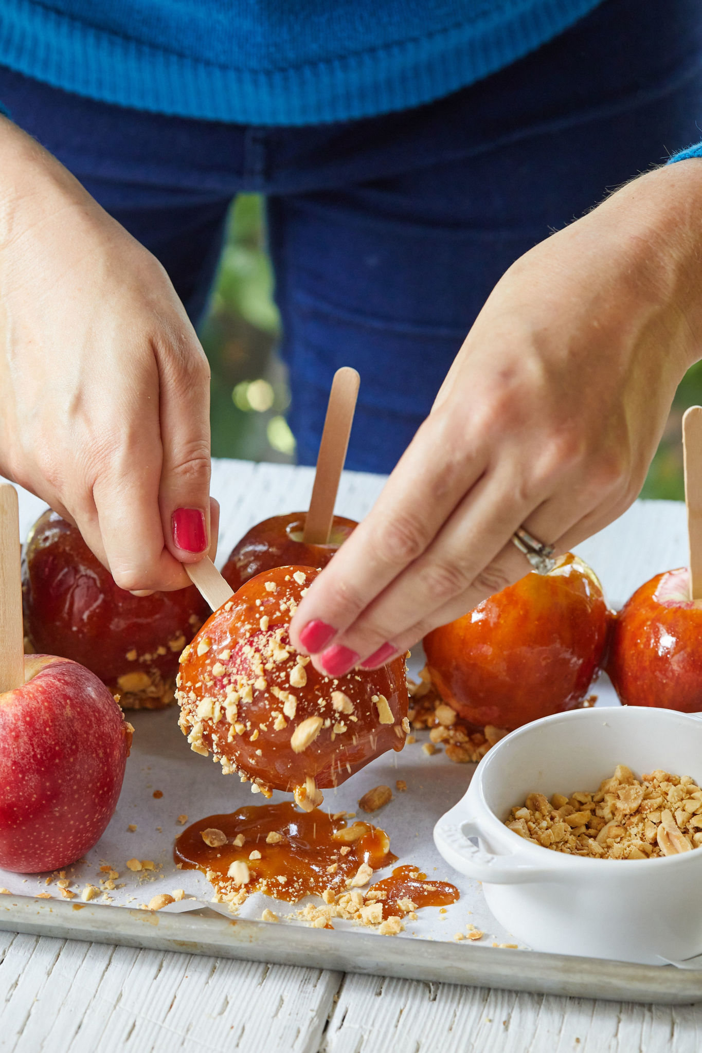 Gemma inserts a popsicle stick into a homemade caramel apple as she tops it with crushed peanuts.