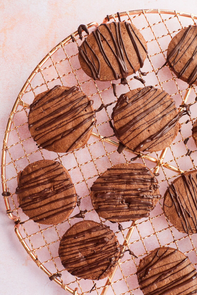 Chocolate shortbread cookies with a chocolate ganache drizzle are presented on a golden wire rack. 