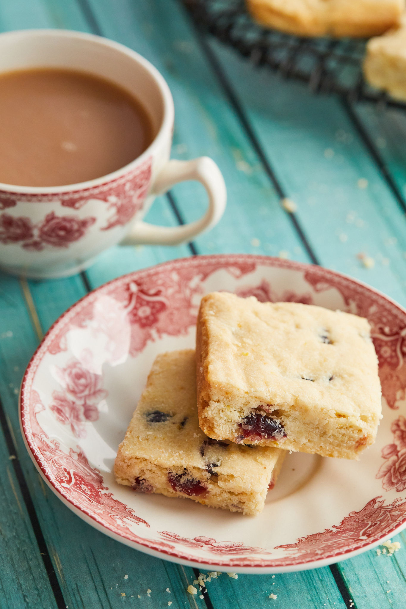 A plate with two servings of cranberry orange shortbread, next to a cup of tea.
