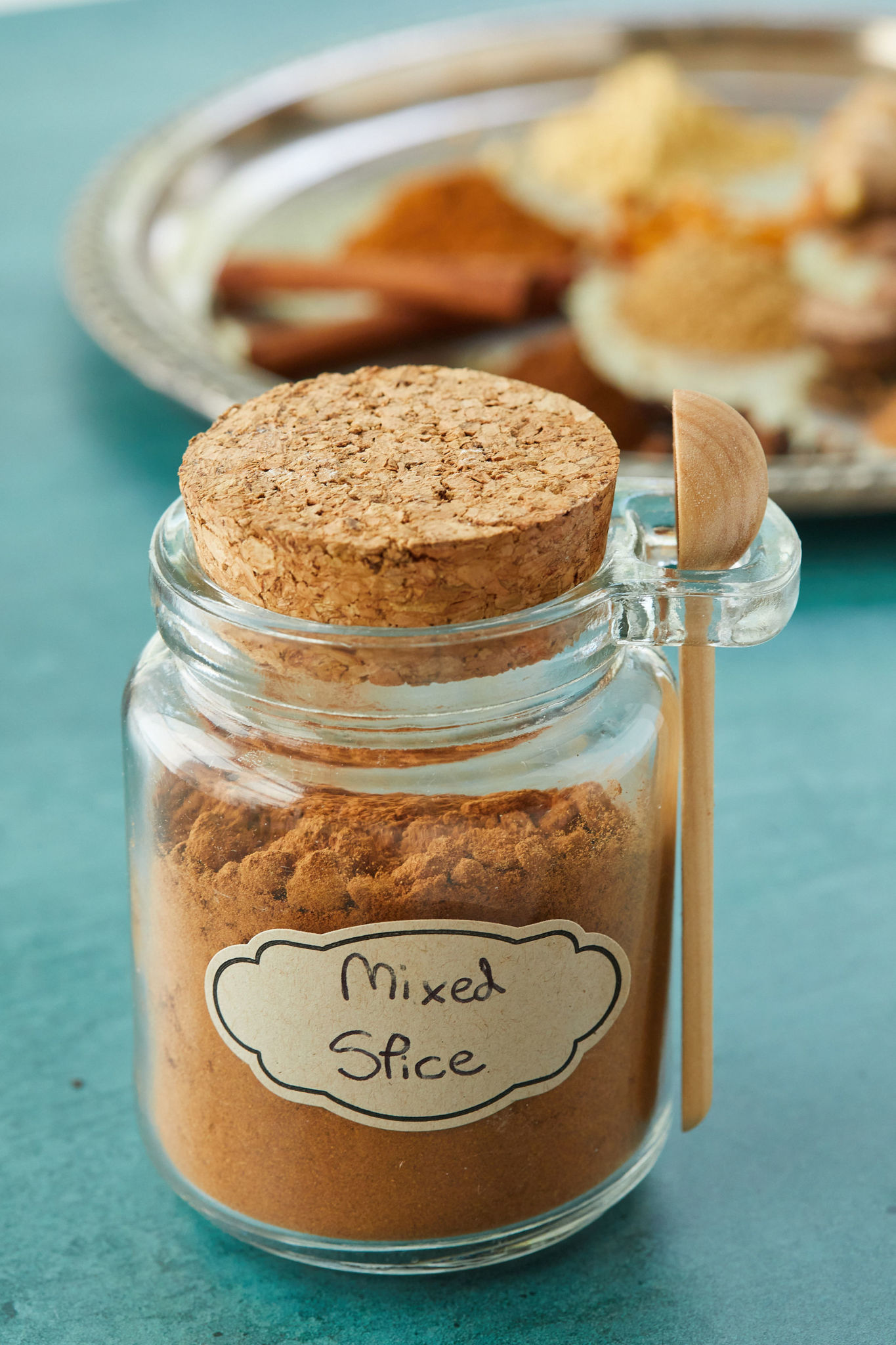 A jar of homemade mixed spice, with a wooden spoon for serving.