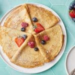Crepe folded into triangle shapes and served with fresh strawberries and blueberries.