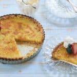Lemon tart with golden crust and filling topped with fresh berries. A slice is cut and served on the side.