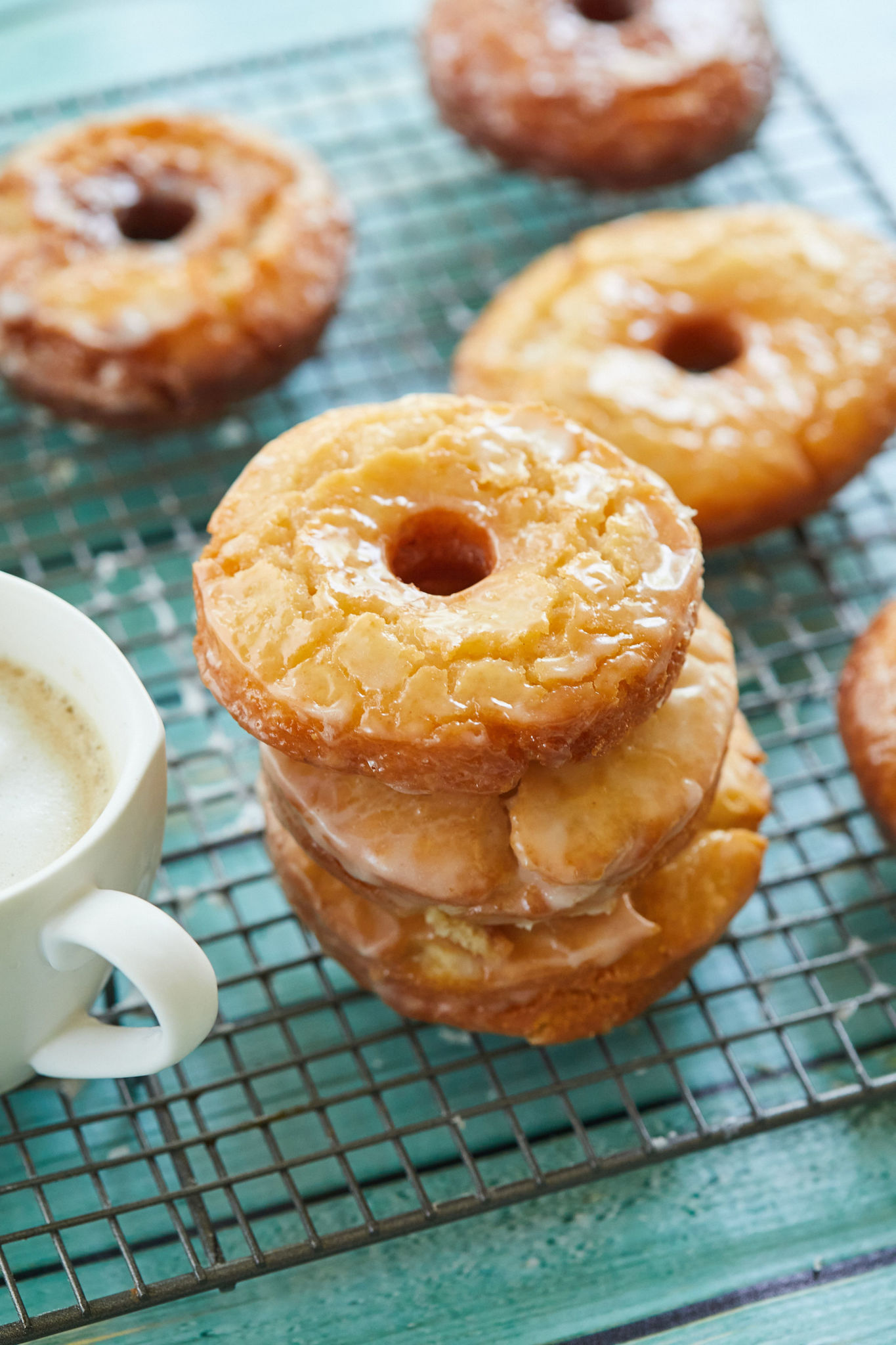 Old fashioned donuts stacked next to a cup of coffee on a cooling rack.