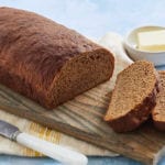 A cutting board with a loaf of pumpernickel bread.