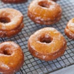 A batch of pumpkin donuts cooling on a rack.