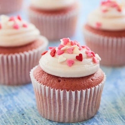 Pink strawberry cupcakes with cream cheese frosting and heart shaped sprinkles on top.