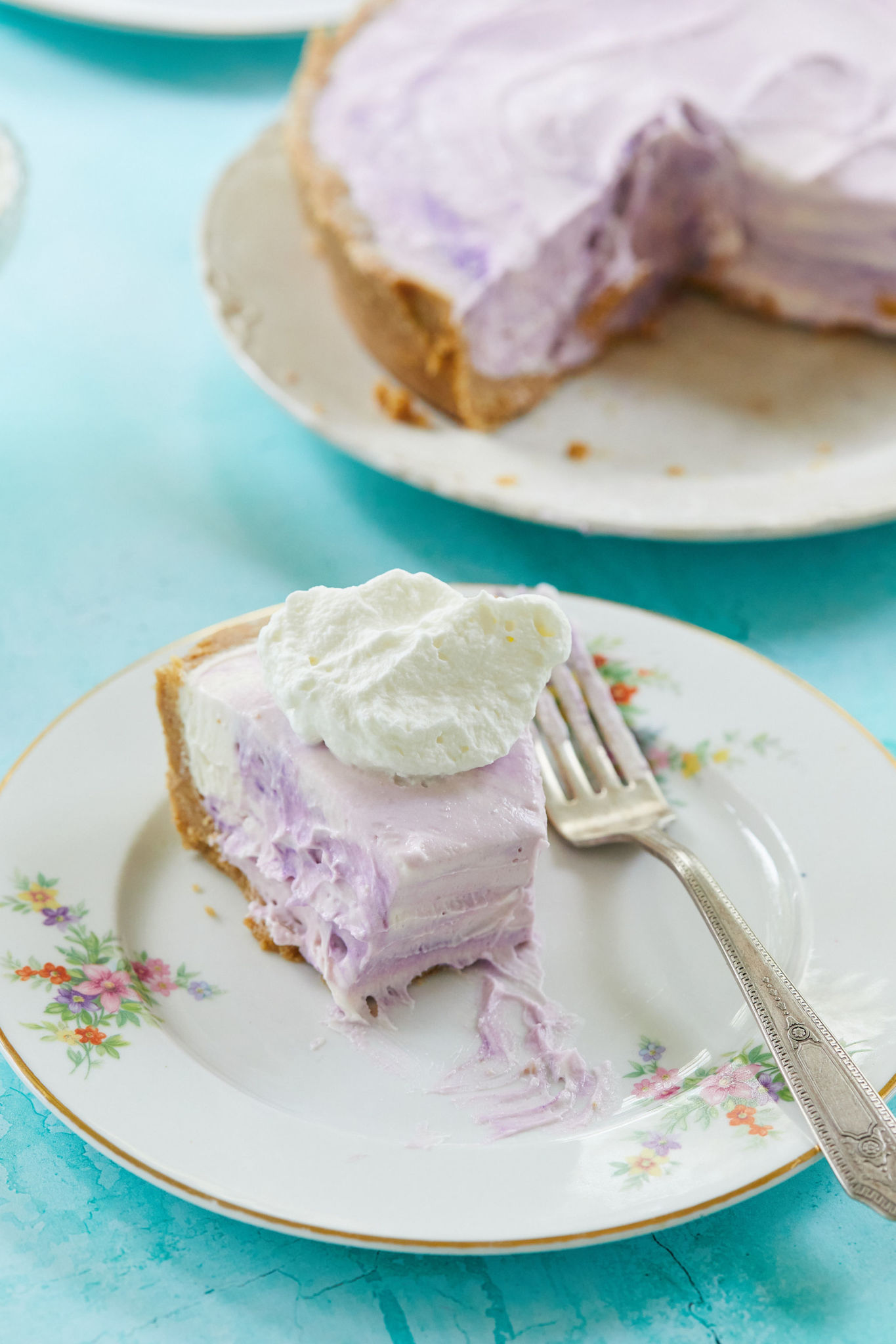 A slice of purple no-bake ube cheesecake with whipped cream on top.