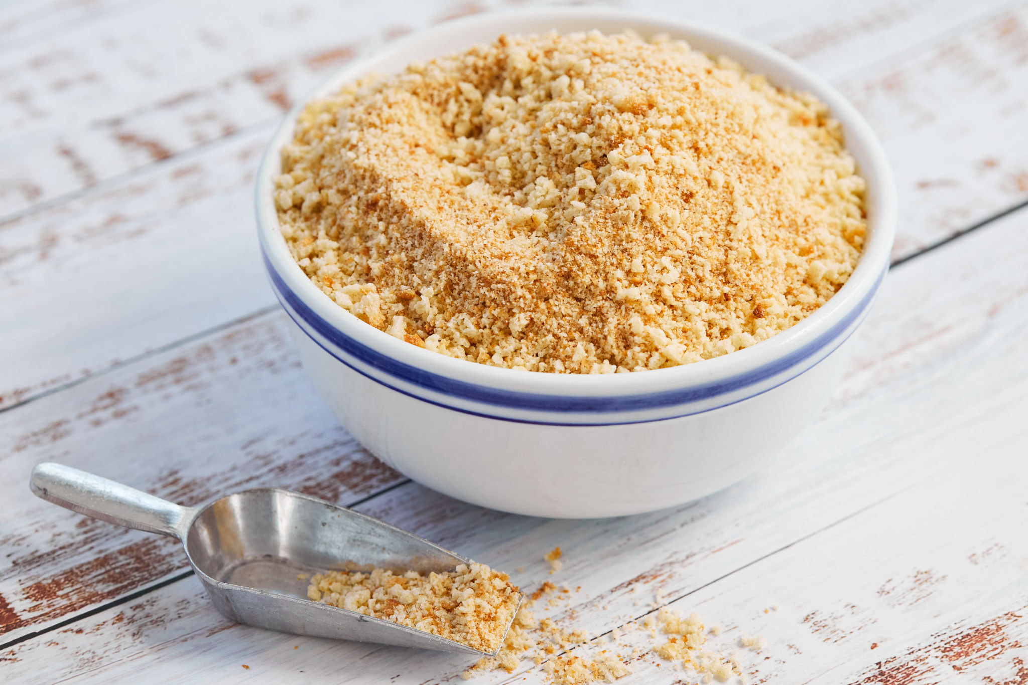A bowl of breadcrumbs with a scoop.