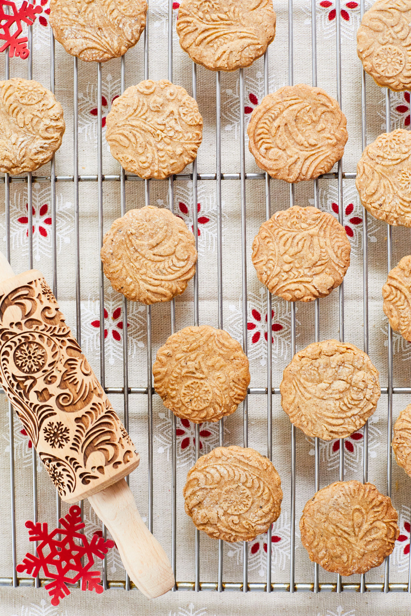 Speculass, beige shortbread with festive designs, rest on a wire rack next to a special Speculass rolling pin.