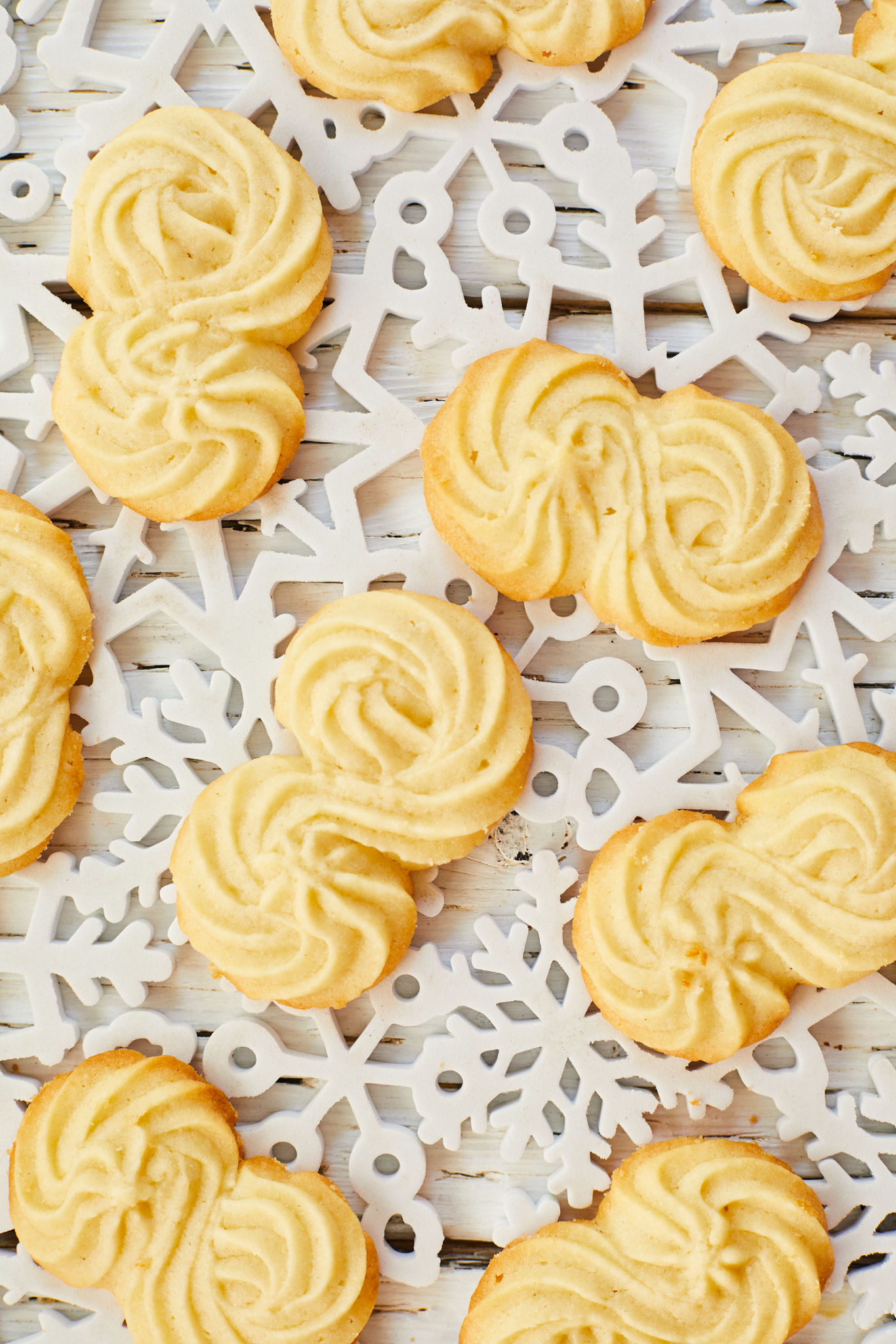 Homemade Sprtiz cookies are presented on a white, snowflake-shaped cutout. 