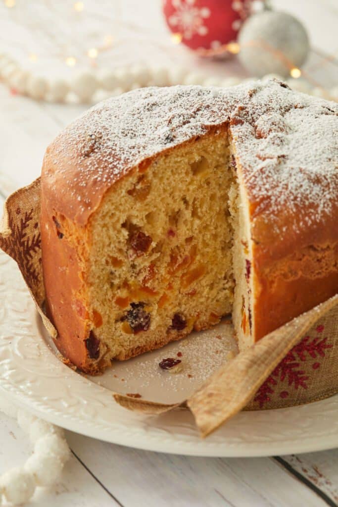 Fluffy Panettone is soft and fluffy, loaded with fruit and candied peels. One slice has been cut off it.