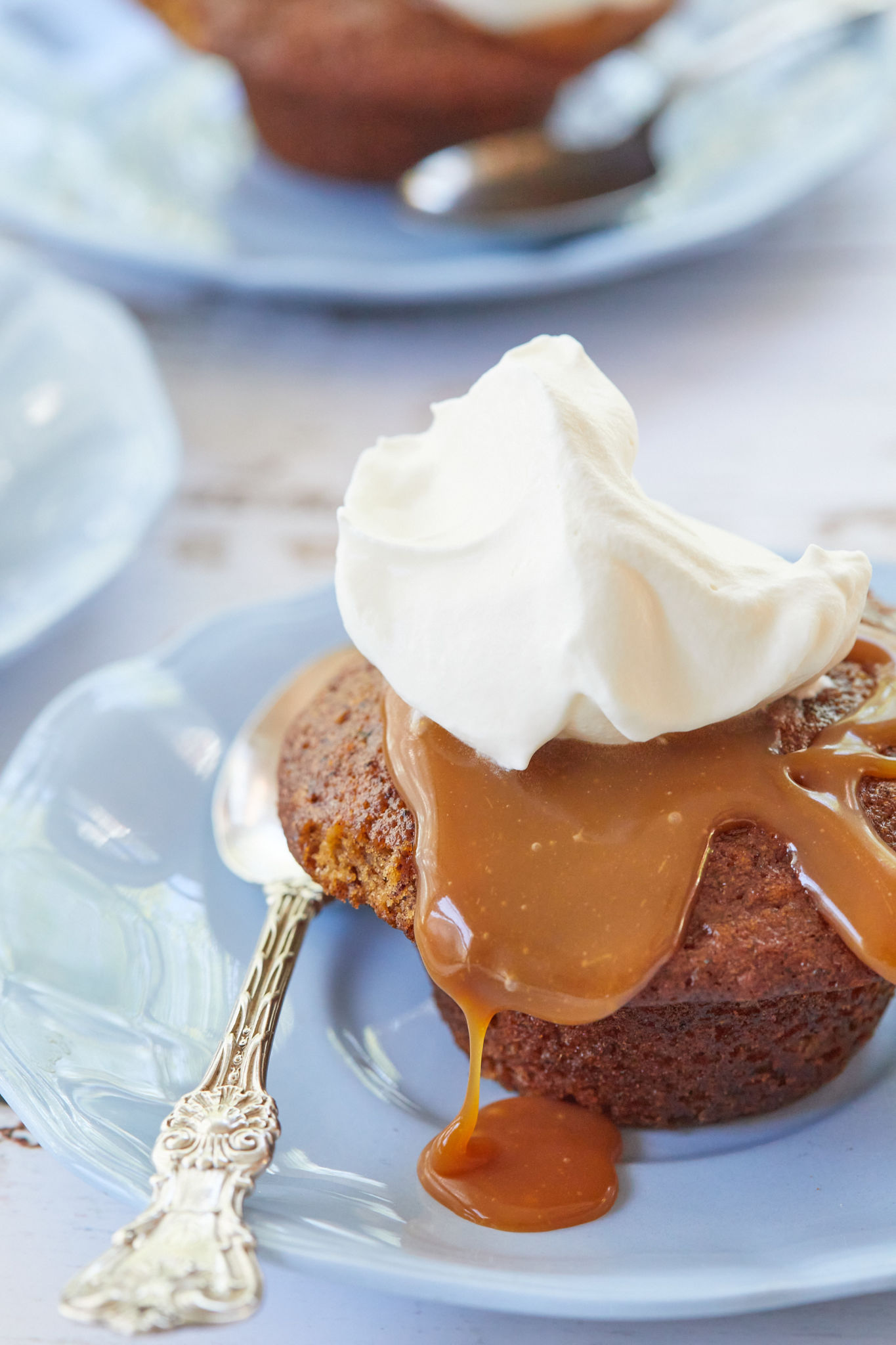 Sticky Toffee Pudding topped with caramel sauce and whipped cream on a blue dish with a spoon.