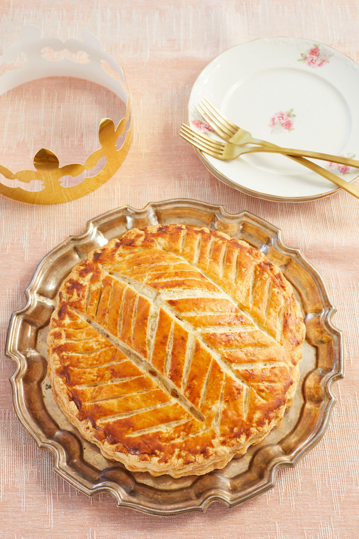 Galette Des Rois, or King Cake, baked next to a crown and plates.