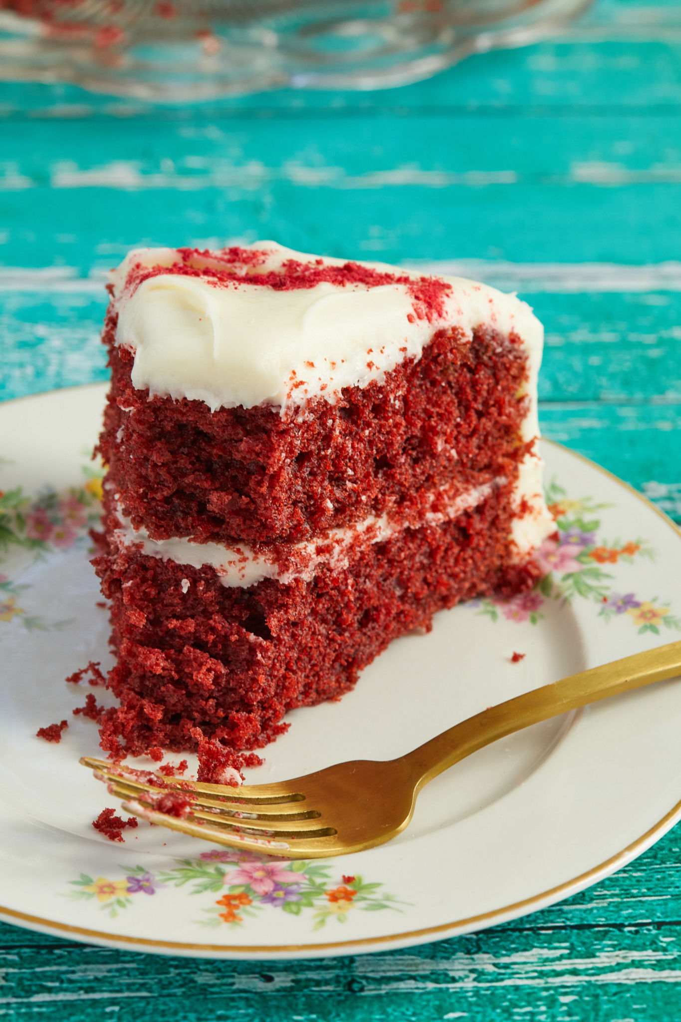 A close up of the interior of a slice of red velvet cake, to show texture and consistency — on a plate with a gold fork.