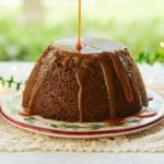 A steamed gingerbread pudding being drizzled with rum sauce.