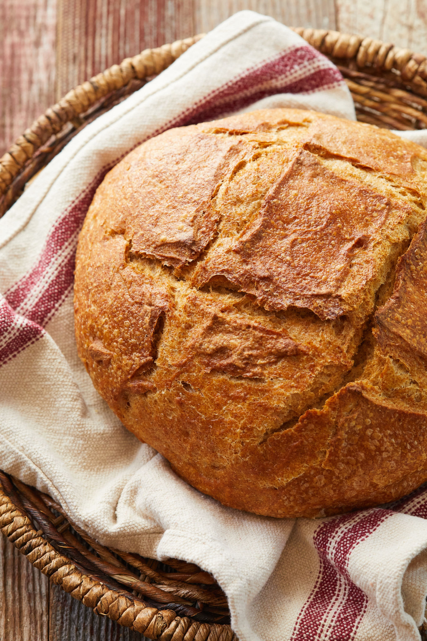 A crusty loaf of Whole Wheat Sourdough Bread in a basket.