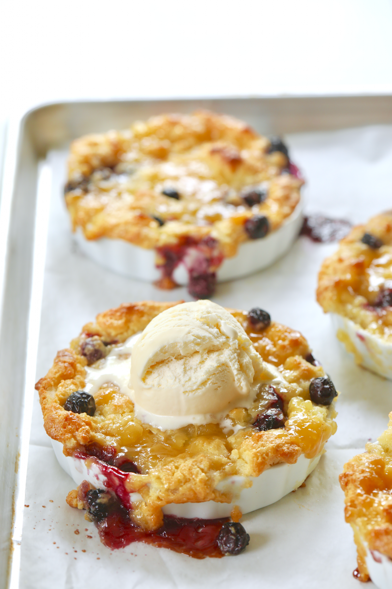 A tray of individual blueberry and lemon bread puddings, topped with ice cream.