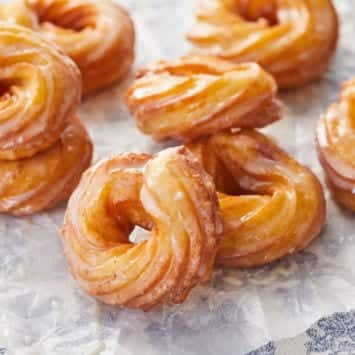 A bunch of lightly fried and glazed French Cruller donuts.