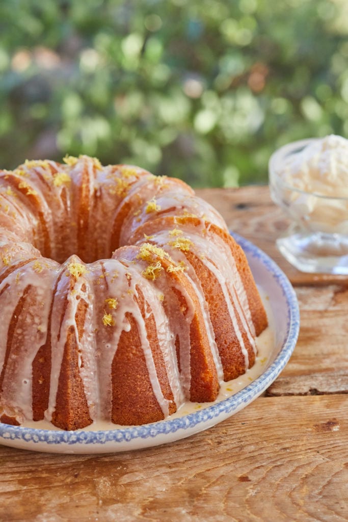 Moist, bright yellow Lemon Pound Cake is glazed and displayed on a big round platter.