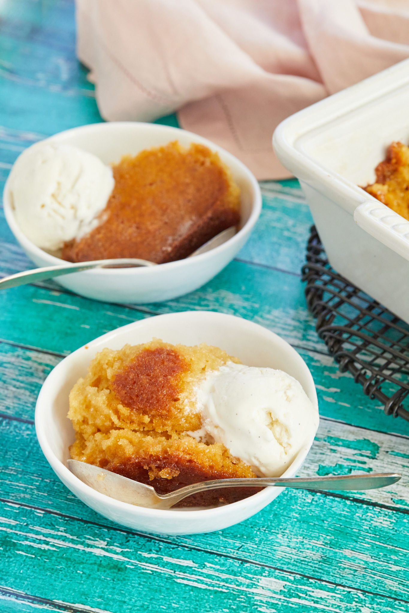 Two bowls of Malva Pudding, served with vanilla ice cream on top.