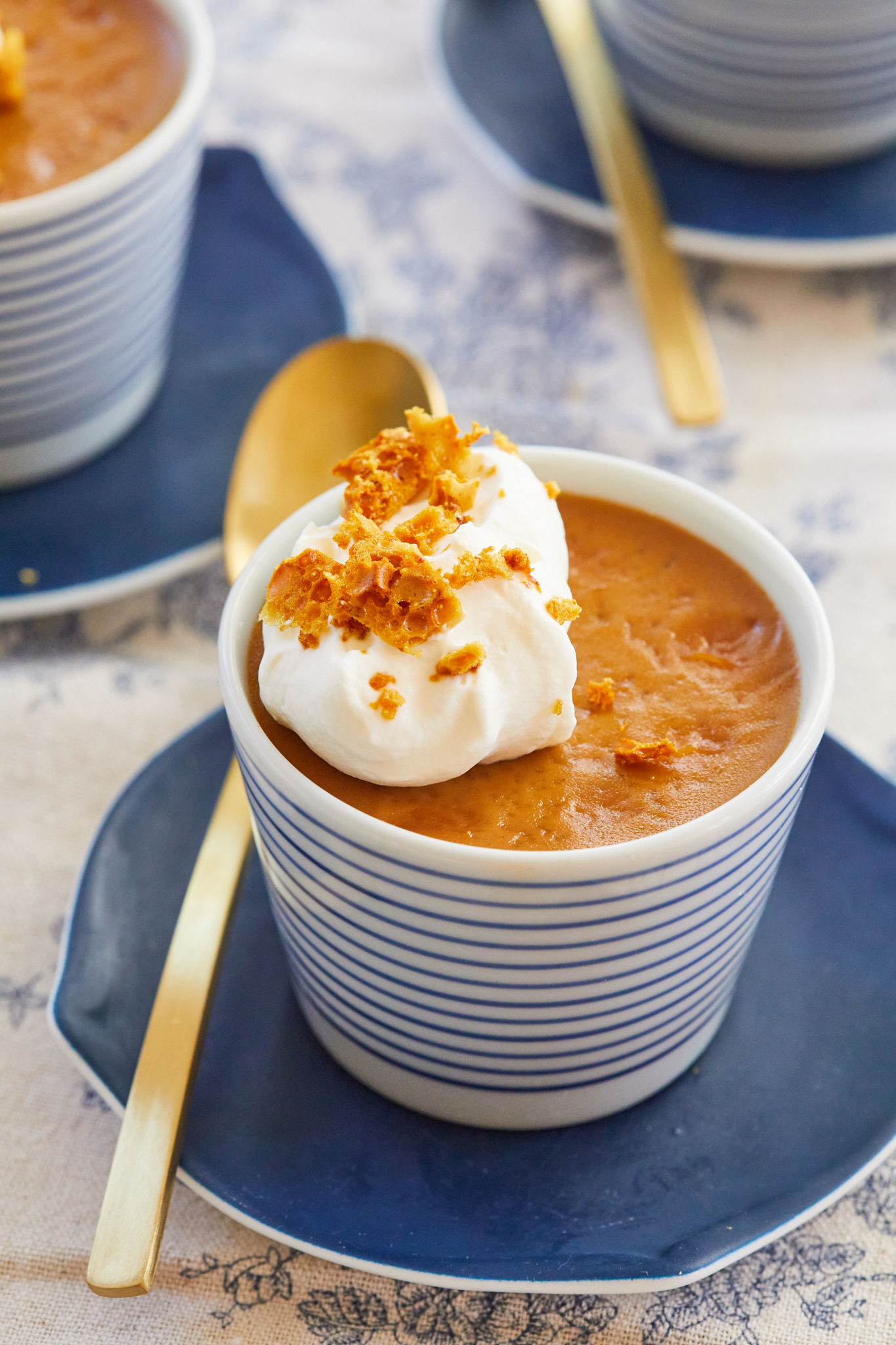 Butterscotch Pot de Creme in a cup, topped with whipped cream and next to a gold spoon.