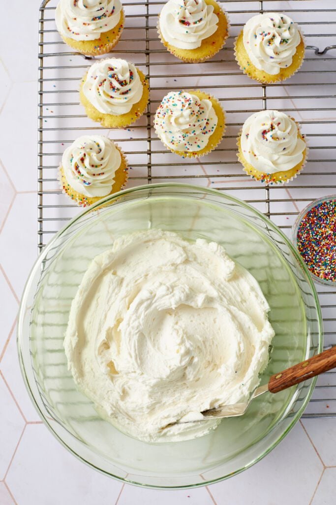 Top down view of a bowl of vanilla buttercream frosting with cupcakes.